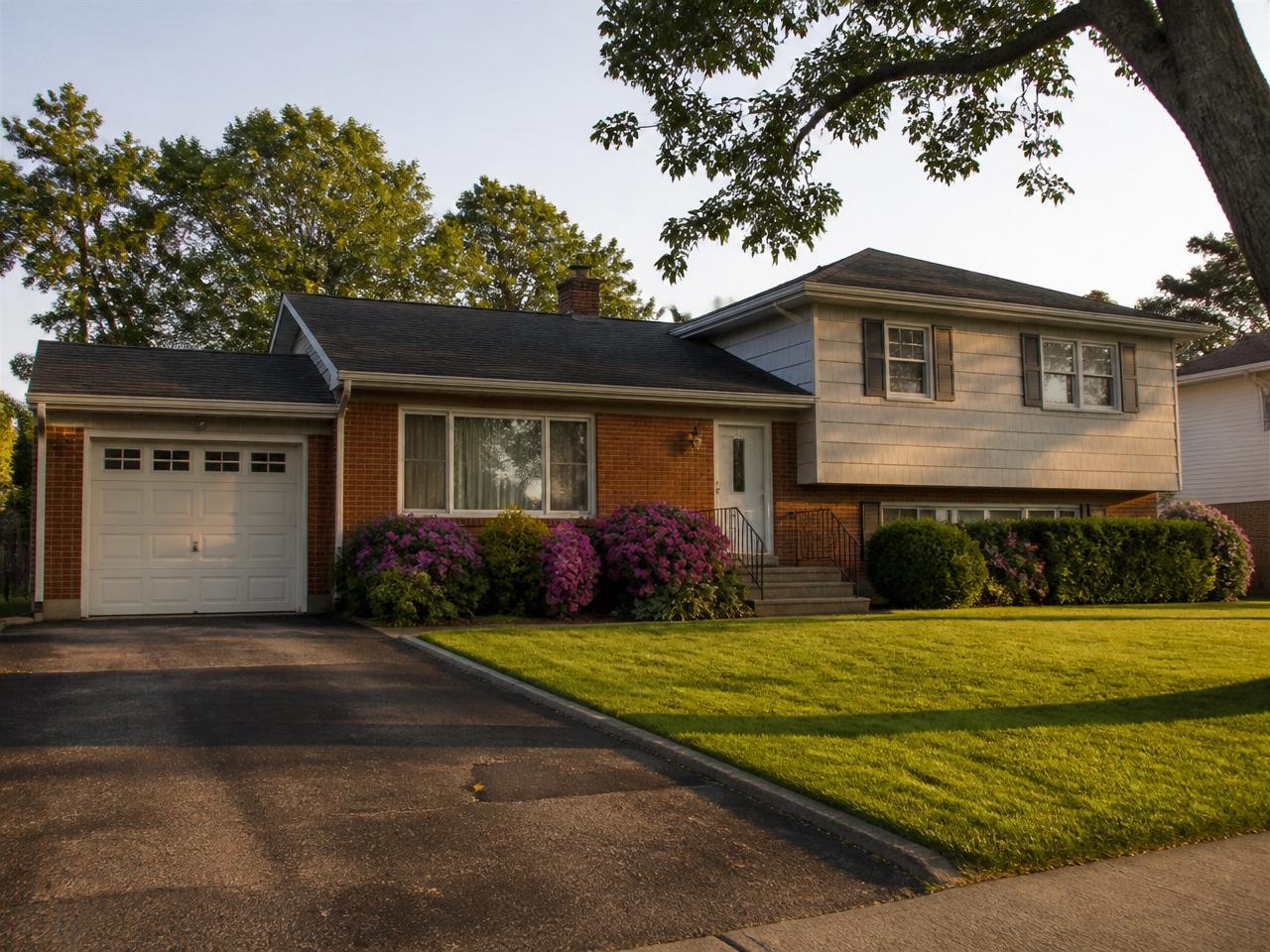 1960s brick split-level home with attached garage and blooming hydrangeas on a suburban Hicksville, NY street