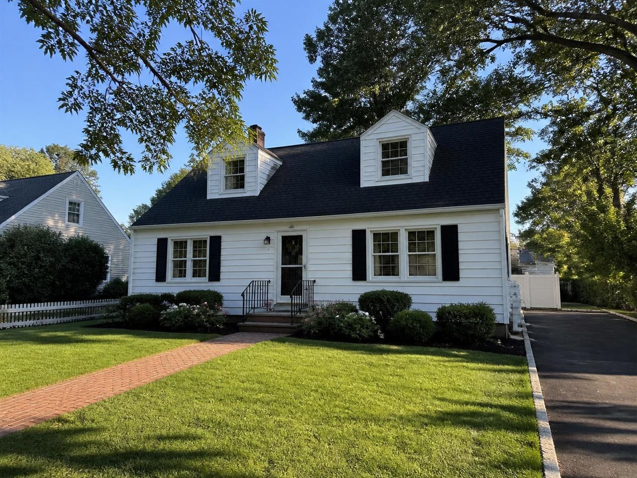 Expanded Cape Cod home with two front dormers, white clapboard siding and black shutters on a quiet Levittown, NY street