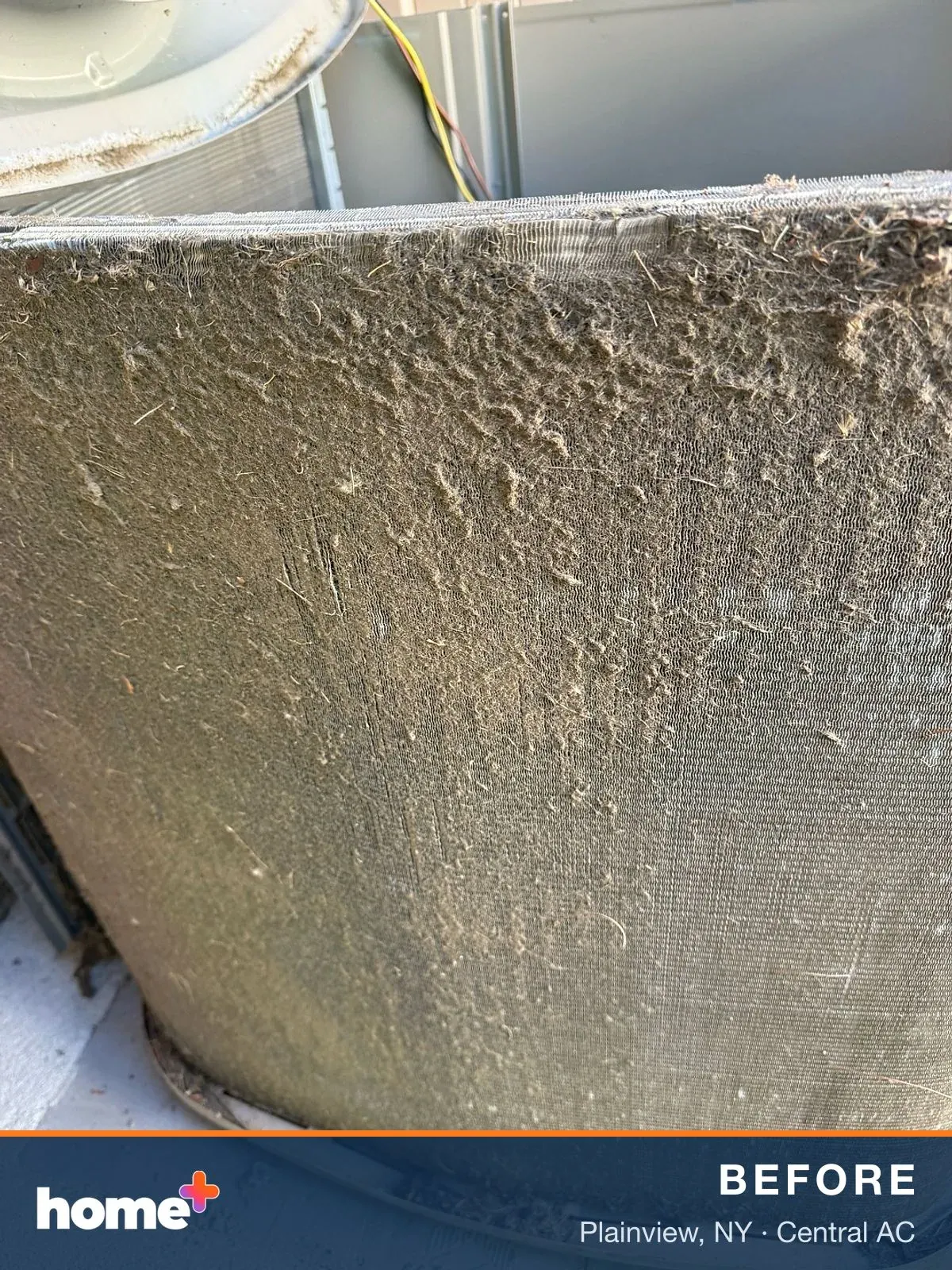 A detailed shot of an outdoor air conditioner coil, completely matted with a thick layer of dirt, lint, and plant fibers.