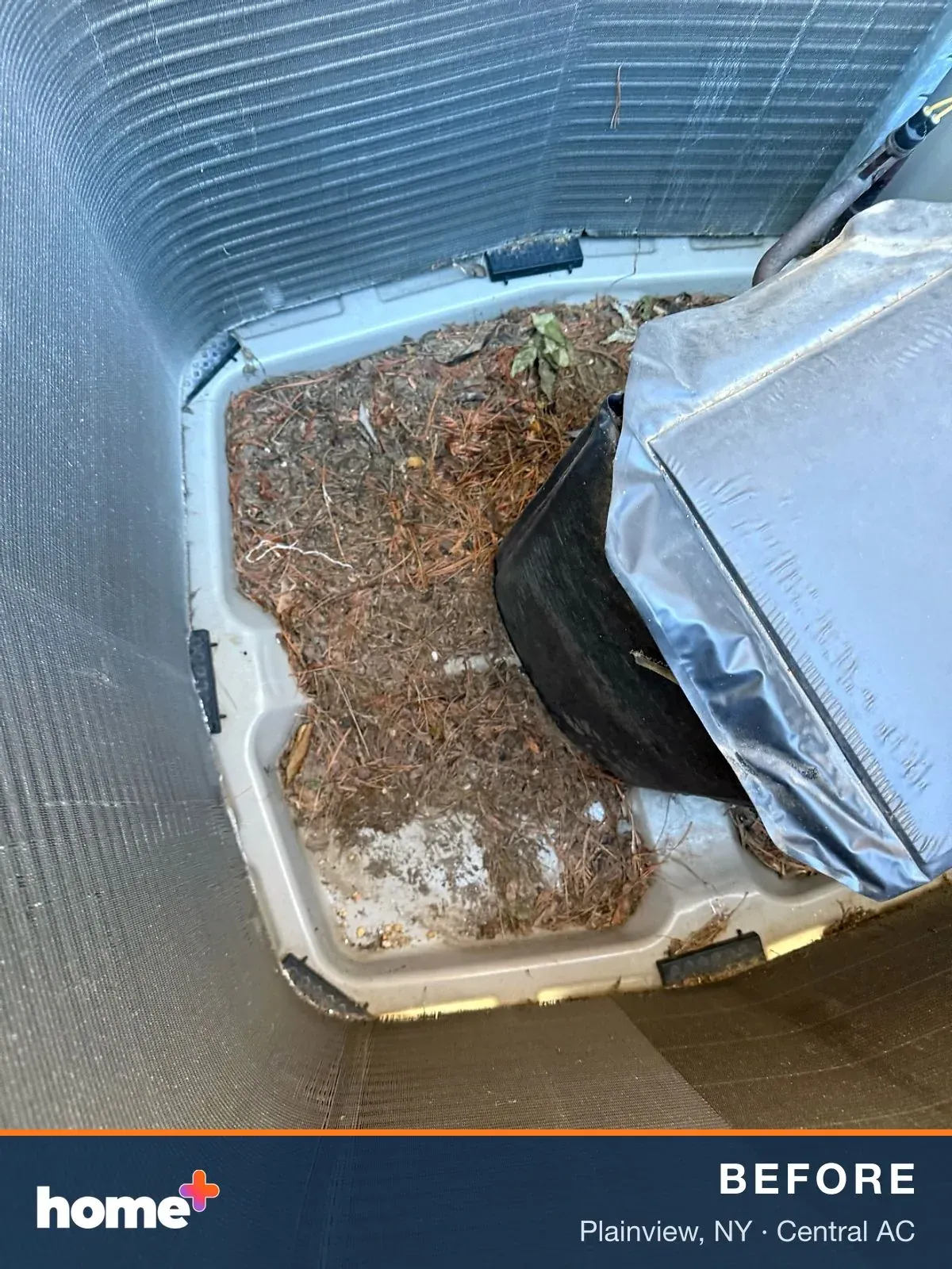 Looking down into an outdoor air conditioner unit, the bottom is filled with a large amount of pine needles, leaves, and natural debris.